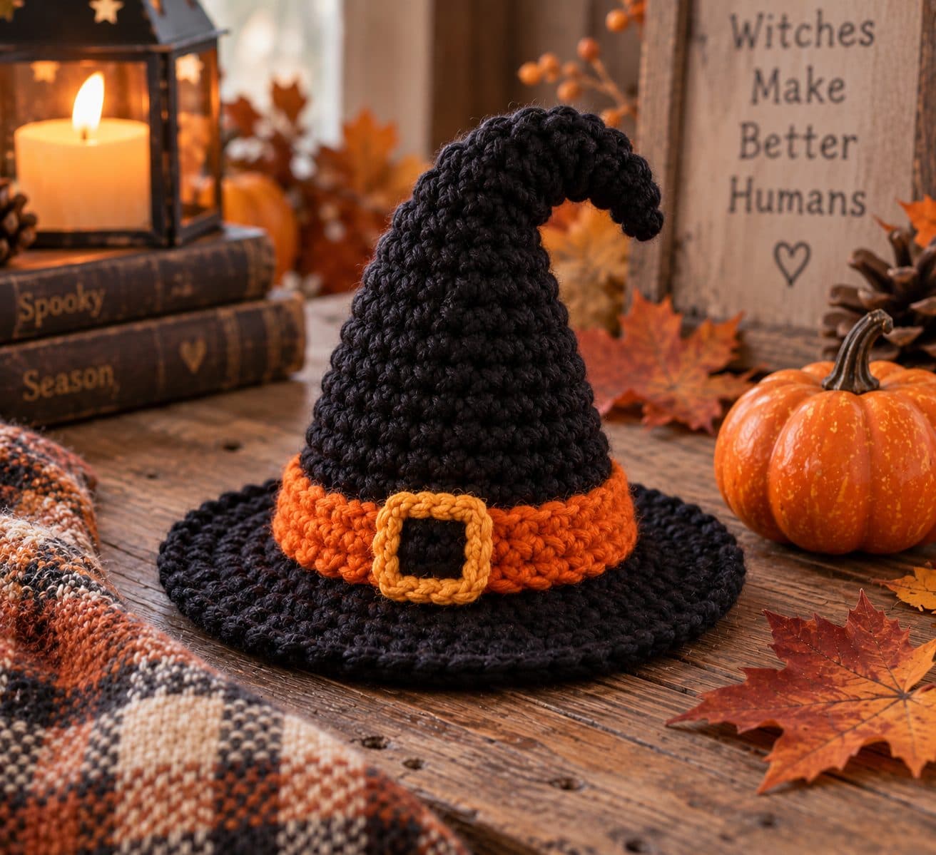 Black crochet witch hat with an orange band and gold buckle among pumpkins and autumn leaves